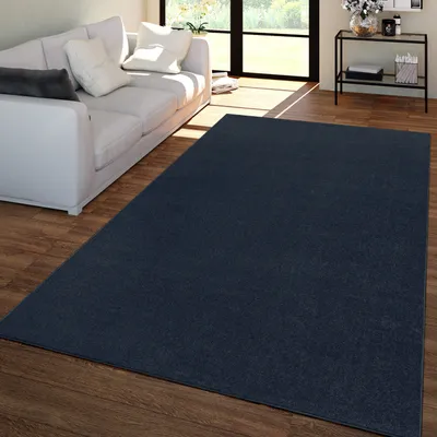 A dark blue rug is placed on a wooden floor in front of a white sofa in a living room.