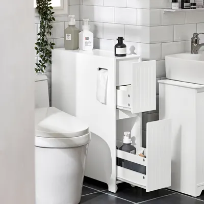 A white slim cabinet next to a toilet in a bathroom.