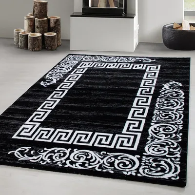 A black rug with a white Greek key and scroll border is displayed on a light gray floor in front of a fireplace.