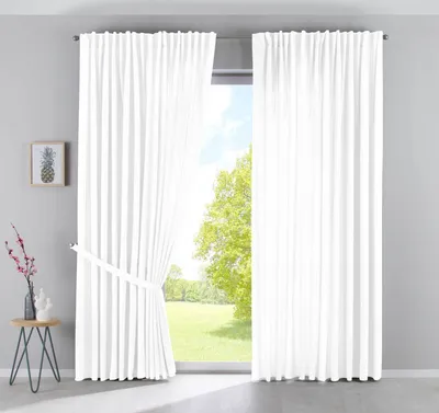 A room interior with white curtains covering a large window, showing a view of trees and a field outside. A small side table with decorative items is placed to the left.