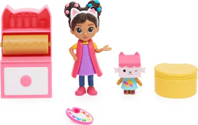 A collection of toys including a doll, a cat figure, a yellow container, and an art studio accessory, arranged on a white background.