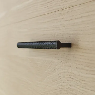 A close-up shot of a black textured drawer pull on a light wood surface.