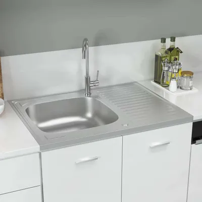 A stainless steel kitchen sink with a draining board is shown installed in a white cabinet.