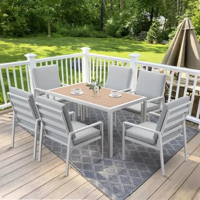 An outdoor dining set on a wooden deck with a green lawn and trees in the background.