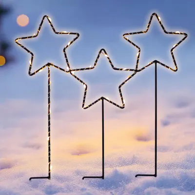 Three illuminated star-shaped garden stakes are planted in the snow.