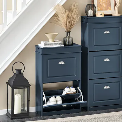 A blue shoe cabinet with shoes inside, placed next to a staircase and a lantern.
