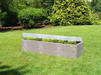 A raised garden bed with plants growing inside, set in a grassy backyard with trees in the background.