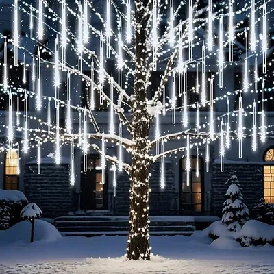 A tree decorated with white meteor shower lights in a snowy yard at night.