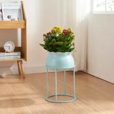 A light blue plant stand with a potted plant on it, placed on a wooden floor next to a wooden bookshelf.