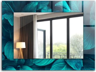 A mirror with a decorative frame of green leaves, reflecting a room with a lamp and a window overlooking trees.