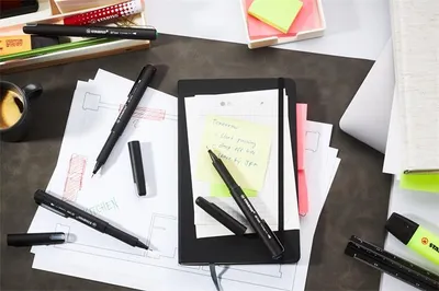 A desk with various stationery items, including pens, notebooks, sticky notes, and papers with diagrams.