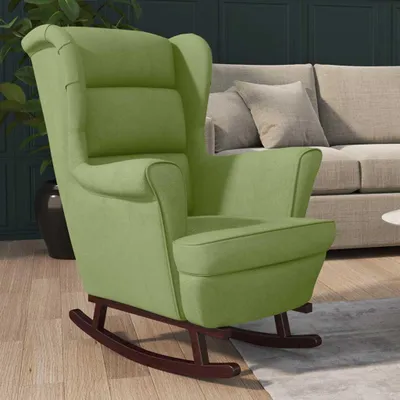 A light green velvet rocking chair is shown in a living room setting, with a sofa and a plant in the background.