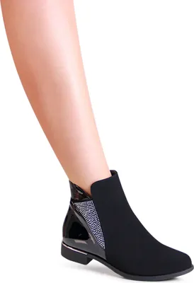 A woman's leg wearing a black ankle boot with glitter and patent leather accents.