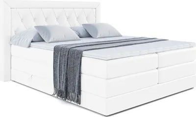 A white boxspring bed with a tufted headboard, two pillows, and a draped blanket.