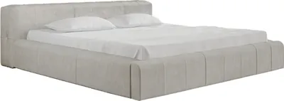 A beige upholstered bed with two pillows and a white sheet.