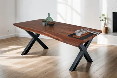 A wooden dining table with a live edge and black metal X-shaped legs, set in a room with wooden floors and white walls.