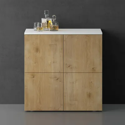 A sideboard or storage cabinet with a white top and wood-grain doors, set against a dark gray wall and light gray floor. Two decanters and glasses with amber liquid are on top.
