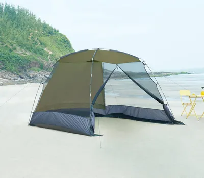 A tent set up on a sandy beach with the ocean and a grassy hill in the background.