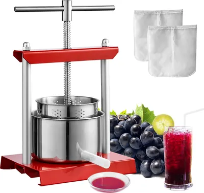 A red and silver fruit press with grapes, a glass of juice, and a small bowl of juice.