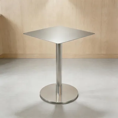 A square stainless steel bistro table with a pedestal base is shown in a room with light wood paneling on the wall and a concrete floor.