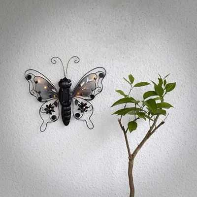 A decorative butterfly with lights on a textured white wall, next to a small green plant.
