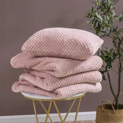A stack of pink blankets and a pillow on a small table next to a plant.