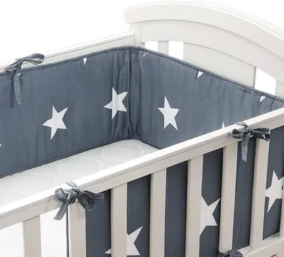 A close-up view of a crib bumper with a star pattern, tied to the crib rails.