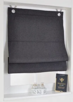 A dark gray Roman blind is shown hanging in a window, partially covering the view. On the windowsill below, there are two small decorative glass bottles and a book.