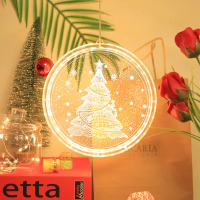 A festive Christmas decoration scene with a lit Christmas tree window light, a small Christmas tree, a jar with fairy lights, and red roses.