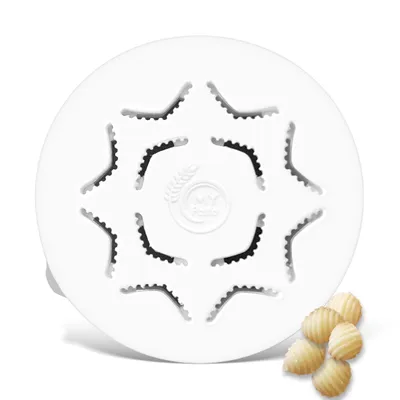 A white pasta maker disc with star-shaped cutouts is shown from a top-down perspective. Several shell-shaped pasta pieces are arranged in the lower right corner of the image.