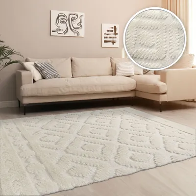 A cream-colored rug with a geometric pattern is placed in a living room setting in front of a sectional sofa.