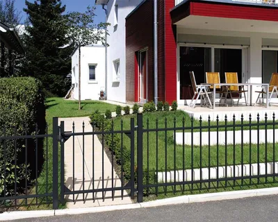 A modern house with a black metal fence and gate in front of a manicured lawn.