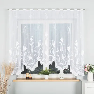 A white lace curtain with a floral pattern hanging on a window.