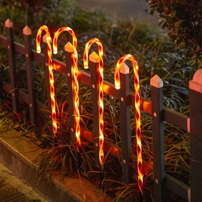 Christmas candy cane lights are attached to a fence in a garden at night.