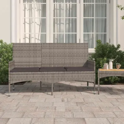A three-seater garden bench with cushions on a paved patio in front of a building with large windows.