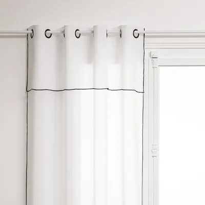 A white curtain with black trim hanging from a curtain rod.
