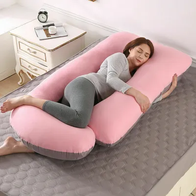 A woman is sleeping on a large J-shaped pregnancy pillow in a bedroom.