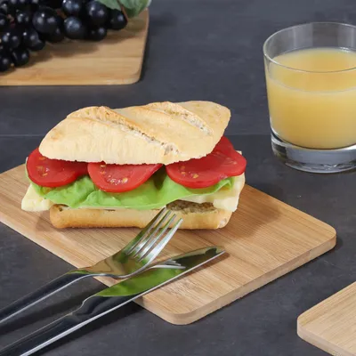 A sandwich and a glass of juice are placed on a wooden board, with grapes in the background.