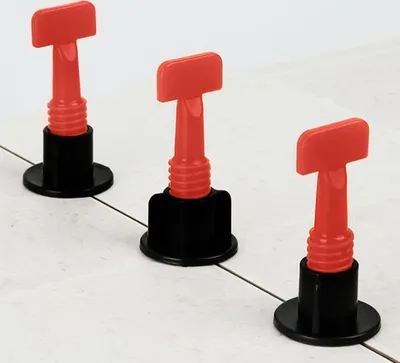 Three red and black tile leveling spacers are placed on a tiled surface.