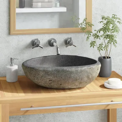 A stone sink on a wooden vanity with a mirror and plant in the background.