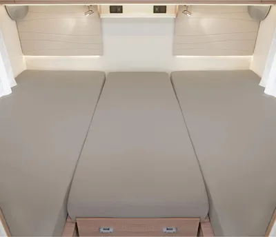 Interior view of a camper or caravan with three beds made up with gray sheets.