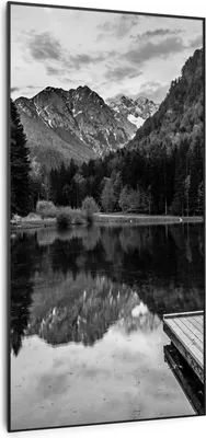 A black and white landscape photo of a lake with mountains and trees reflected in the water.