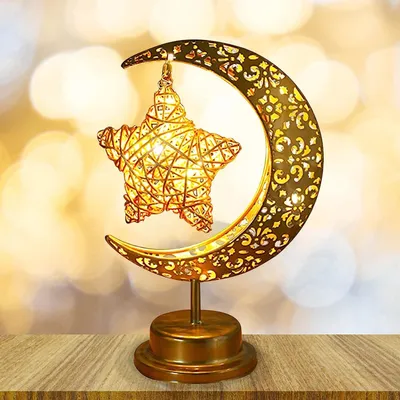 A decorative golden lamp shaped like a crescent moon holding a star, placed on a wooden surface with a bokeh background.