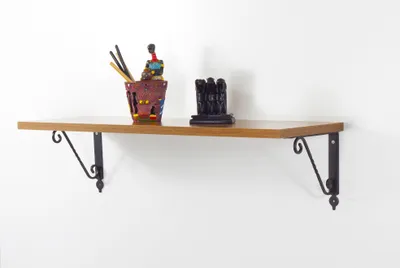 A wooden shelf mounted on a white wall, decorated with a small sculpture and a pot of art supplies.