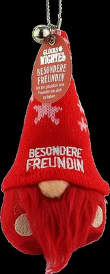 A red gnome plush toy with a bell and a tag, against a black background.