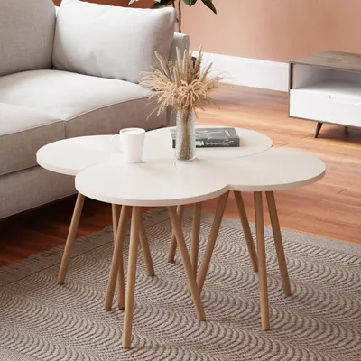 A set of nesting coffee tables with a vase of dried flowers and a book on top, placed on a rug next to a sofa.