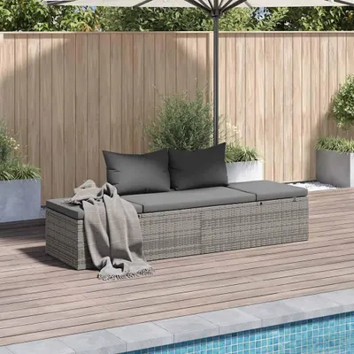A grey rattan garden bed with cushions and a throw blanket is placed on a wooden deck next to a swimming pool.