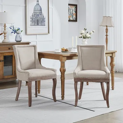 Productafbeelding van Set van 2 eetkamerstoelen van A&A Furniture, met verstevigd stoffen bekleding, trale houten poten, bronzen nagels en een beige kleur.