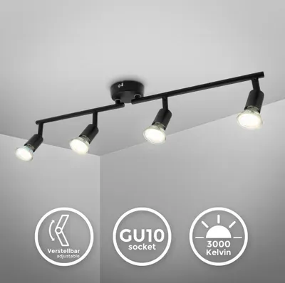 A black four-spot ceiling track light fixture is shown against a white ceiling and gray wall.