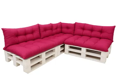 A sectional sofa made from white wooden pallets with pink cushions, shown against a white background.